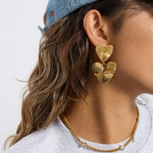 Close-up of golden ribbed heart-shaped earrings on model with radiating texture detail