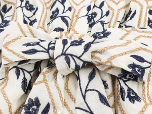 Nahaufnahme der Vintage-Blumenstickerei mit Schleifendetail am cremefarbenen Kleid