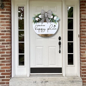 Rustic round wooden Welcome sign with bow and greenery hanging on a white front door