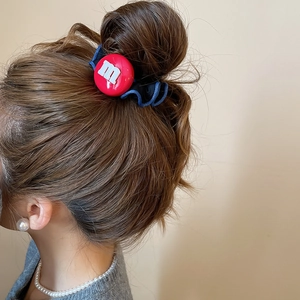 Détail du chouchou en tissu avec breloque lettre m rouge sur un chignon élégant