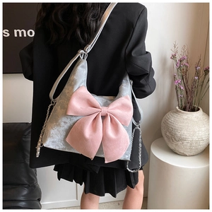 Detail of silver textured shoulder bag with a large pink bow and metal chain strap