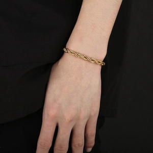 Close-up of a gold twisted rope chain bracelet worn on a wrist with intricate texture