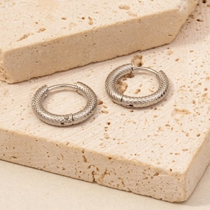 Macro detail of silver hoop earrings featuring intricate snake scale texture on metal surface
