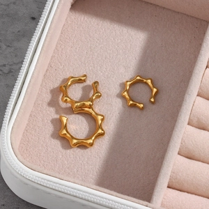 Detailed view of 18K gold plated serrated ear cuffs on a soft pink velvet background