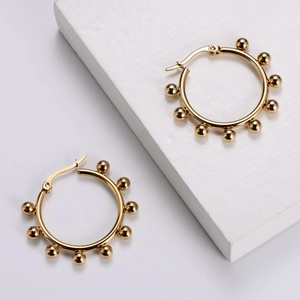 Detail of golden stainless steel hoop earrings with small bead accents on stone