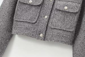 Detail of grey boucle jacket showing textured fabric and embossed silver metal buttons