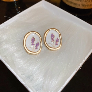 Detailed close-up of oval lavender floral earrings with golden frames on a white plush mat