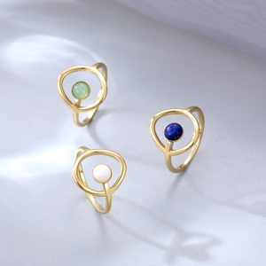 Anillos geométricos dorados con lapislázuli, jade y perla en superficie gris suave