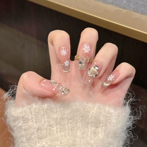 Detail of Christmas press-on nails with snowflakes, pearls, and diamonds on a plush background