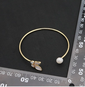 Detailed top view of gold butterfly bracelet with white pearl and measuring ruler