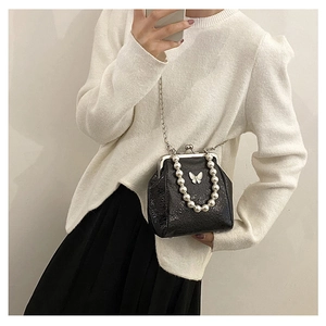 Detail of black glossy crossbody bag with pearl handle, chain strap and butterfly logo