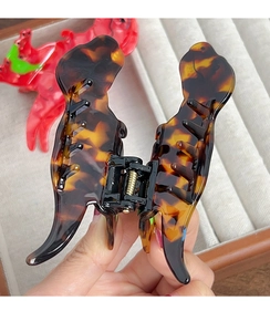 Close-up of tortoise shell pattern acetate dinosaur hair claw clip held by hand