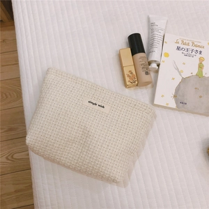 Macro detail of cream woven fabric makeup bag with a Simple Wish label on white bedding
