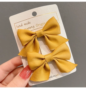 Close-up of two yellow satin bow hair clips on handmade card for girls hair styling