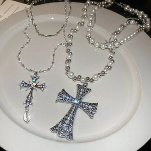 Detail of layered silver cross necklaces with sparkling crystals and pearl beads on white tray