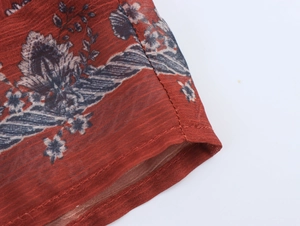 Detailed macro view of reddish-brown floral chiffon fabric with neat stitching