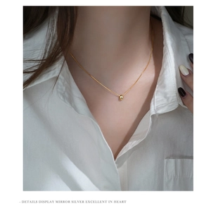 Close-up of minimalist gold bean pendant necklace on model with white shirt