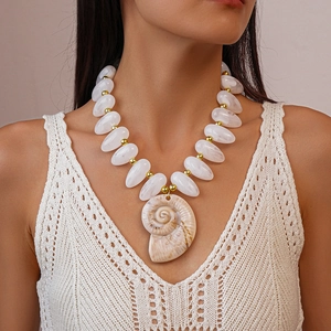 Detail view of a shell pendant necklace with acrylic white beads and gold accents on a model