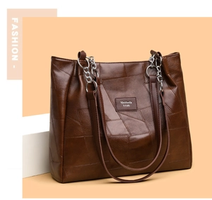 Detail of dark brown PU leather tote bag featuring geometric patchwork and metal chain