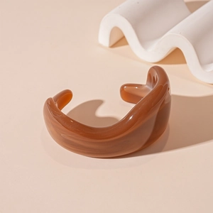 Detailed view of amber acrylic open bangle featuring a natural marble pattern on warm background