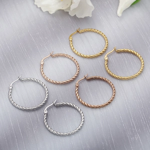 Detail of three pairs of twisted hoop earrings in gold, rose gold and silver finish