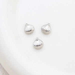 Detailed view of three silver shell-shaped pendants with small loops on white ceramic