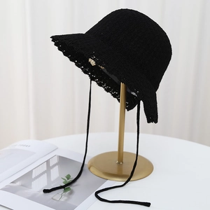 Close-up of black knitted bucket hat with lace-up bow and scalloped edge on gold stand