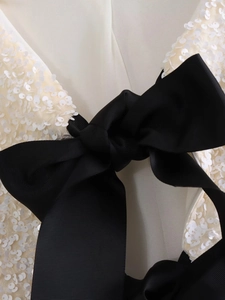 Detail of white sequin fabric with black grosgrain bow and intricate stitching