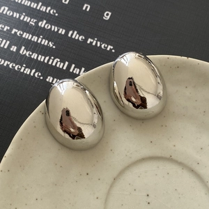 Detailed close-up of shiny oval bean earrings with a mirror finish on a ceramic tray