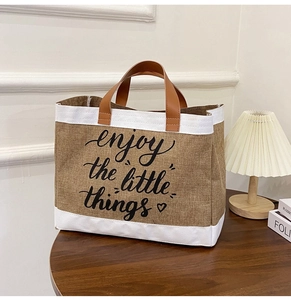 Detail of jute tote bag with enjoy the little things text on dark wood table