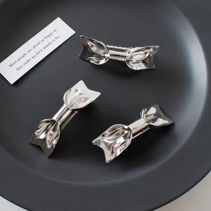 Three silver metal bow hair clips on a black plate with minimalist elegant design