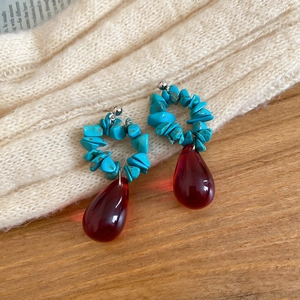 Detail of ethnic beaded drop earrings with blue stone and red crystal on a wooden table