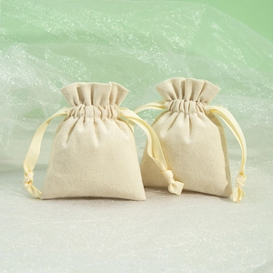 Beige cotton linen jewelry pouches with ribbon drawstring on decorative green background