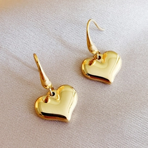 Polished 14k gold heart-shaped drop earrings with 3D design on a beige silk background