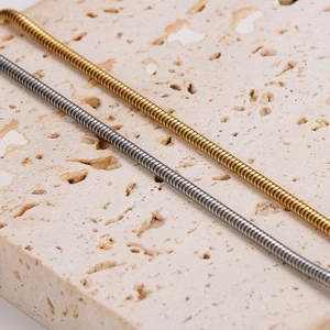 Sleek gold and silver snake chain bracelets displayed on a cream travertine stone