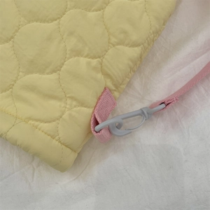 Détail du sac fourre-tout matelassé jaune avec anses roses et un crochet en plastique gris