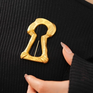Macro detail of vintage keyhole brooch in matte gold finish on black knit sweater