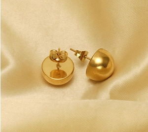 Macro view of gold hemisphere stud earrings on elegant golden silk satin background