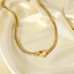 Detail of gold-plated heart pendant on a flat Cuban snake chain over white silk