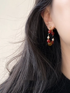 Detail view of tiger eye and pearl beaded hoop earrings on model with retro design