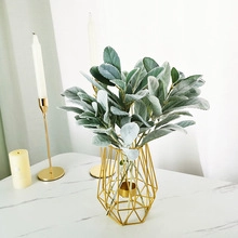 Close-up of artificial flocked leaves in a gold geometric hollow iron vase on marble