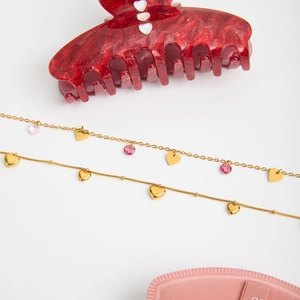 Flat lay of pink jewelry box with 18K gold butterfly necklace and red glitter hair claw