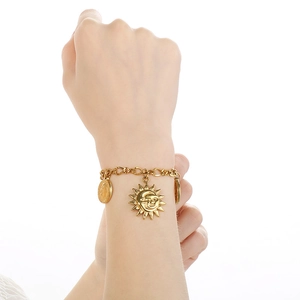 Close-up of gold chain bracelet with sun, moon, and coin charms worn on wrist