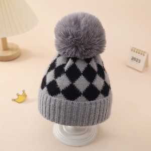 Close-up of winter baby knit hat with grey plaid pattern and large fluffy pompom detail
