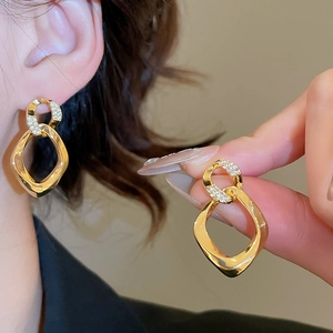Detail of twisted gold geometric drop earrings with sparkling cubic zirconia pavé