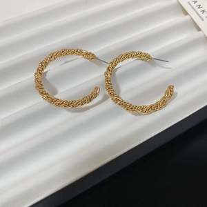 Close-up detail of golden twisted rope C-shaped hoop earrings with silver pins