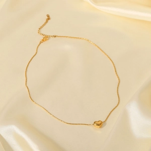 Detail view of a 18K gold plated heart pendant necklace on soft beige silk fabric