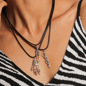 Three Gothic skeletal hand and skull pendants on black leather cords worn by a model