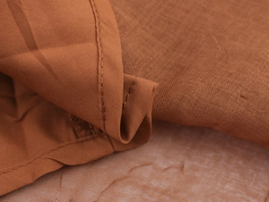 Detailed close-up of brown fabric texture and fine stitching on a V-neck maxi dress