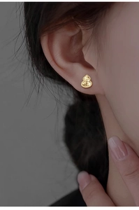 Macro shot of gold-plated hulu earrings featuring a shimmering textured surface on the ear